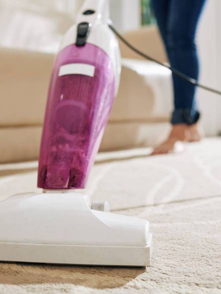 Close-up image of woman vacuum cleaning carpet in main room of her house
